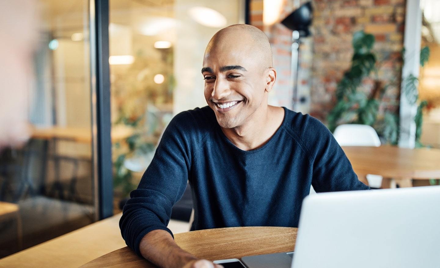 Man with shaved head smiling in front of a laptop