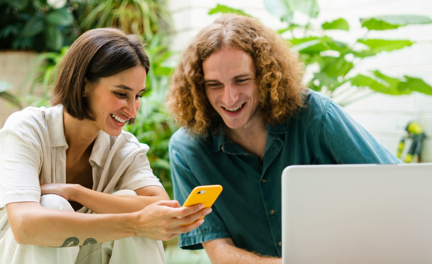 Two coworkers comparing data on laptop and phone