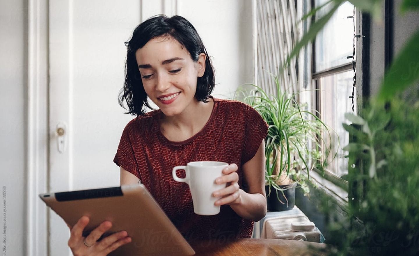 Woman in red shirt holding tablet and mug