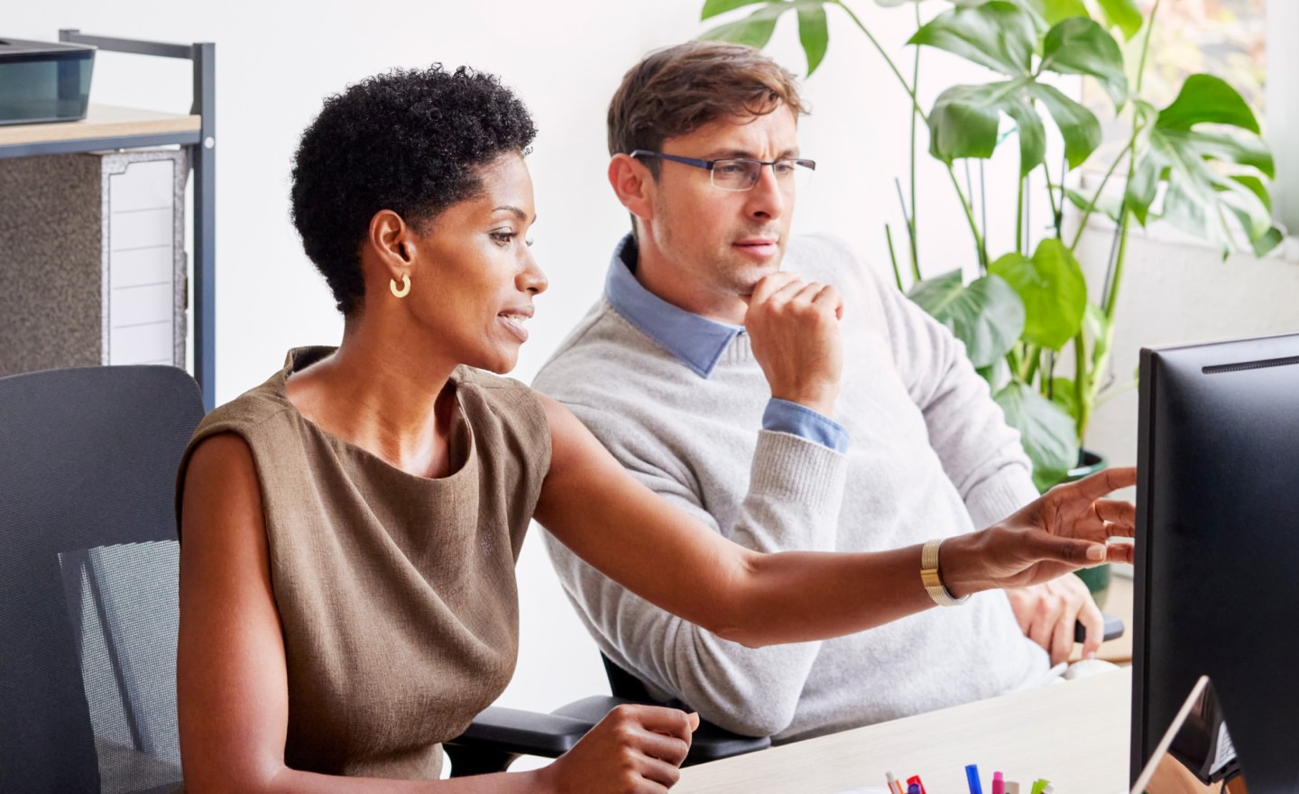 Woman pointing at screen while man wearing glasses looks