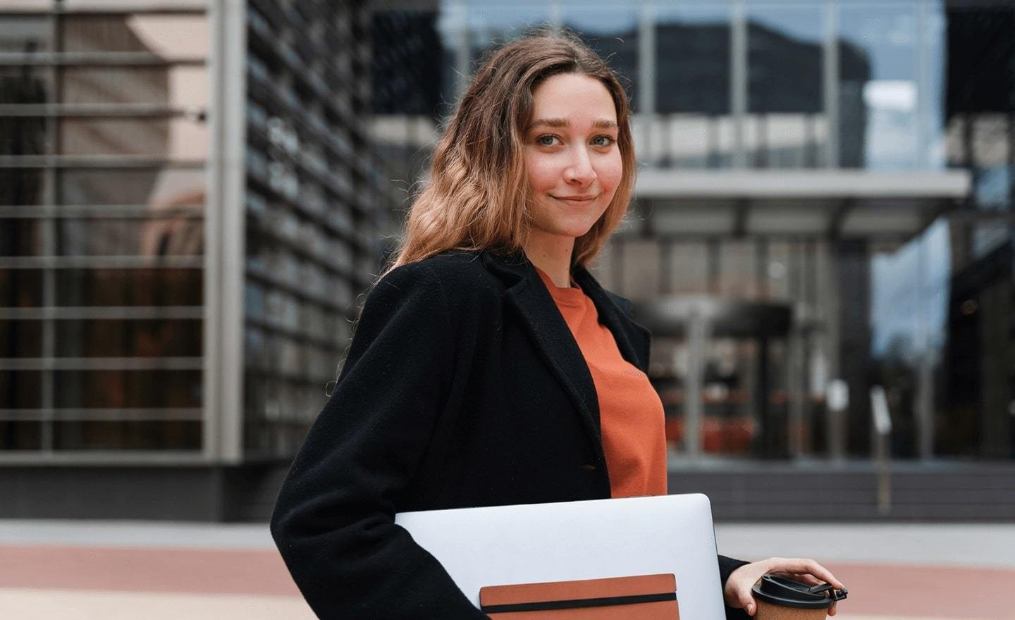 Women outside looking at camera with coffee and laptop in hand