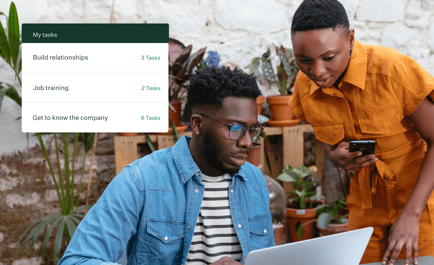 Photo of two people looking at a computer screen near a shelf with plants