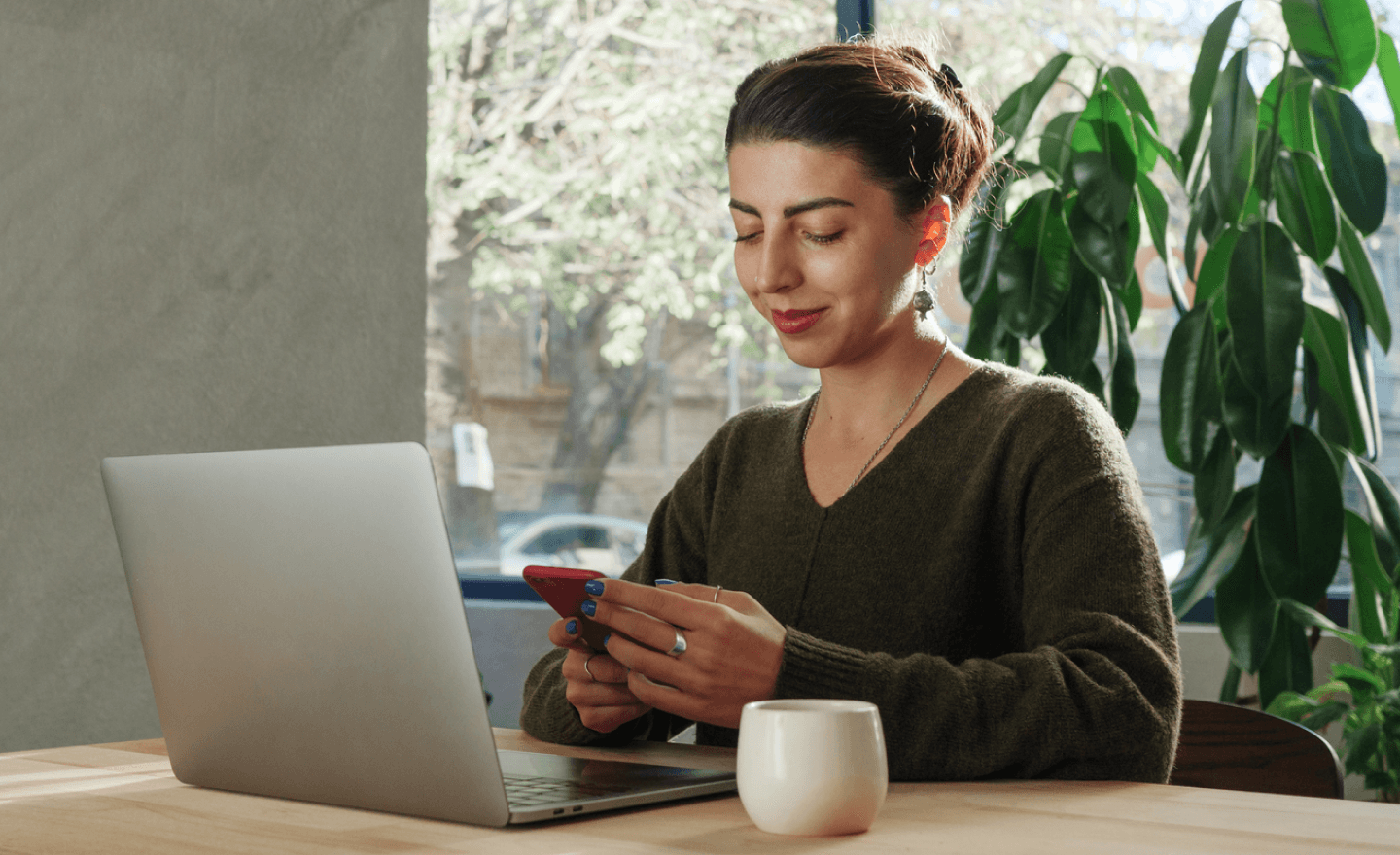 Woman sitting behind a laptop reviewing a doc on her phone smiling